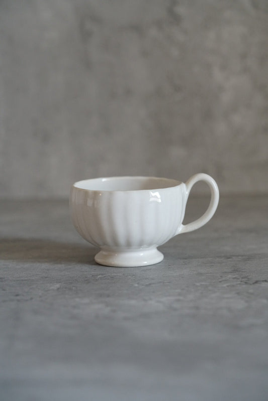 Small white footed tea cup with fluted sides and a slim curved handle.