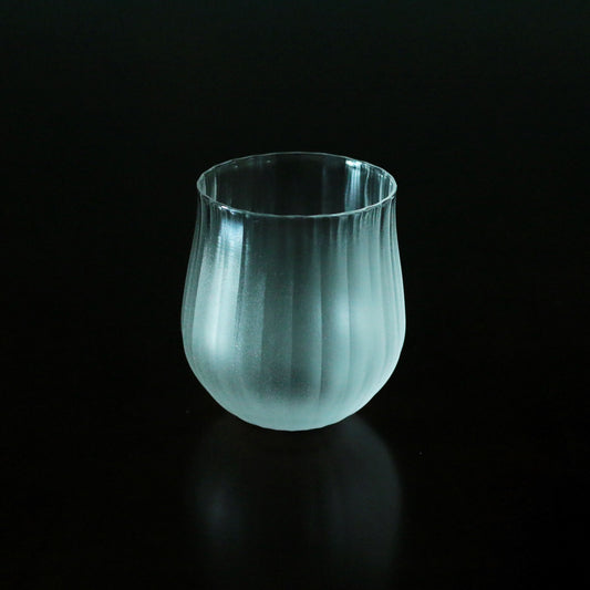 Softly ribbed glass tumbler in pale sea green, glowing against a dark background.