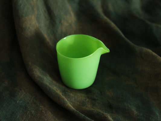 Small opaque glass pourer in bright grass green with a drawn lip, on dark green cloth.