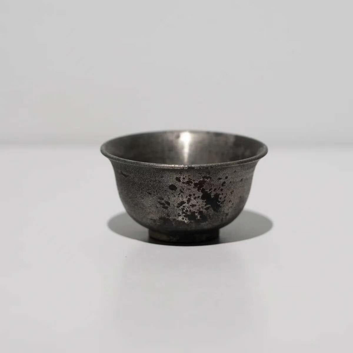 Small footed cup in dark tarnished silver-grey with a mottled, weathered surface.