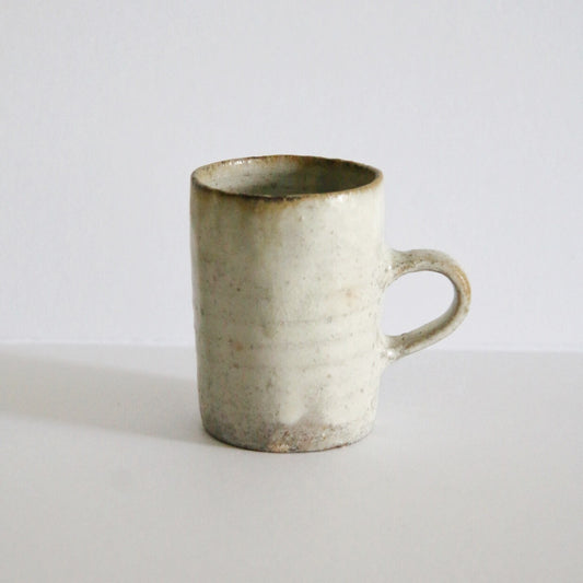 Tall cream mug with a rust-marked base and a small loop handle, lit against white.