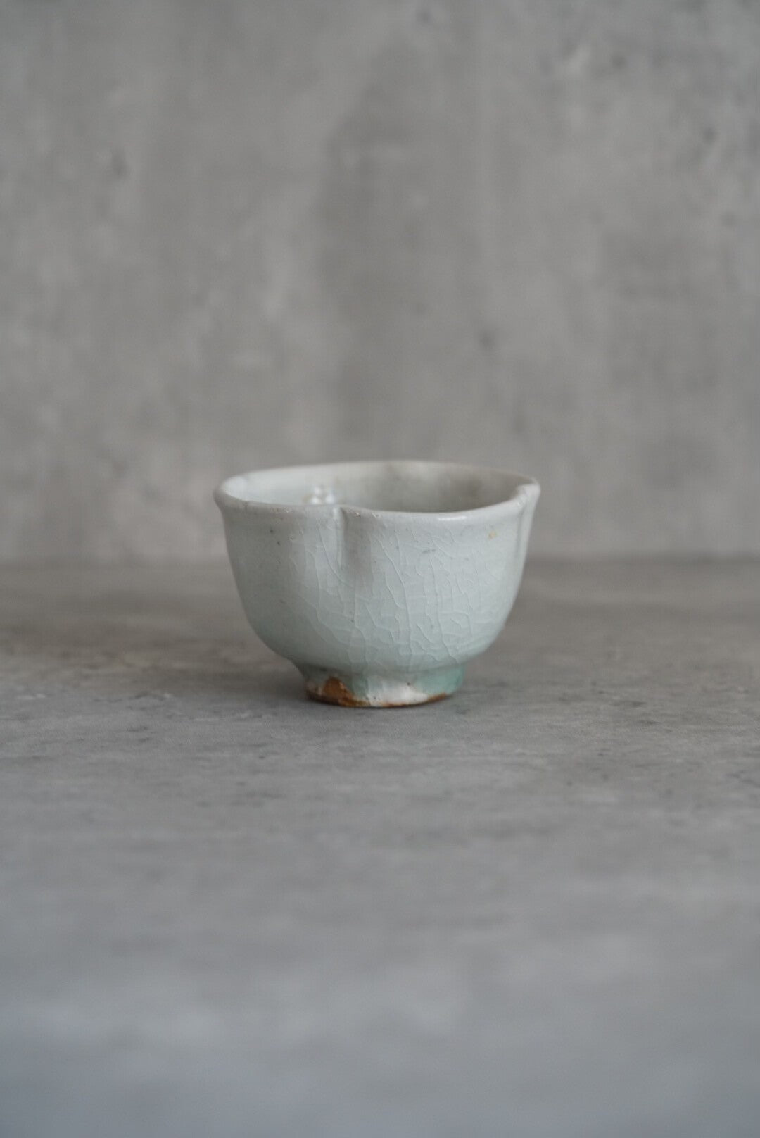 Small footed cup in pale sea green with a softly waved rim, on grey concrete.