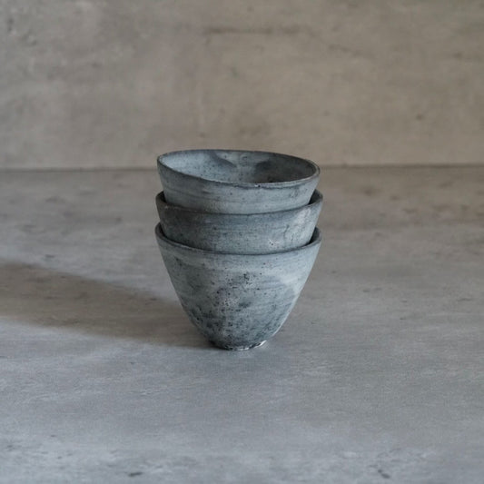 Three small grey cups stacked in a leaning tower, their surfaces rough and mottled.
