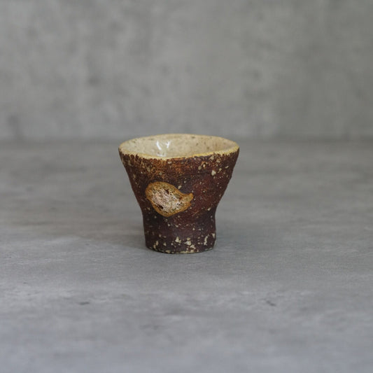 Small flared cup with a rough bark-like brown outer wall and a pale glazed interior.