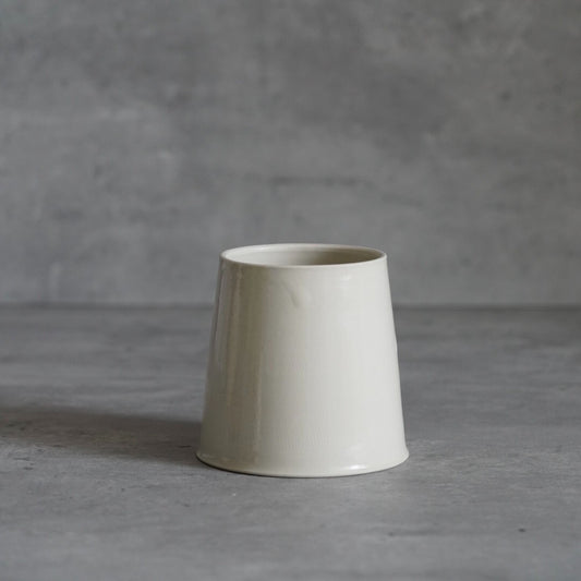 Tall conical cream cup with a smooth matte surface, standing on pale grey.