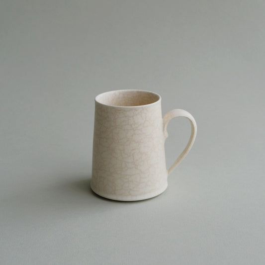 Tall plain cream mug with a finely crackled glaze and a slim loop handle, on grey.