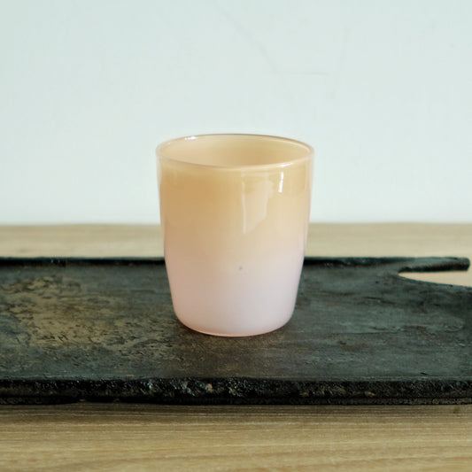 Opaque glass cup in soft peach cream, standing on a dark weathered board.