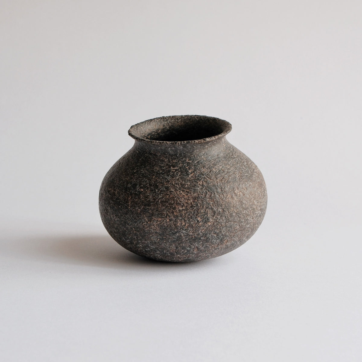 Small round-bellied vase in matte earth brown with a coarse sandy surface and a short neck.