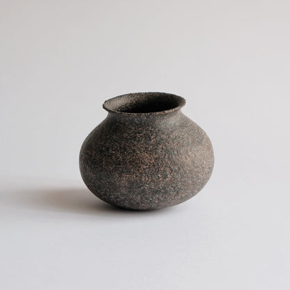 Small round-bellied vase in matte earth brown with a coarse sandy surface and a short neck.