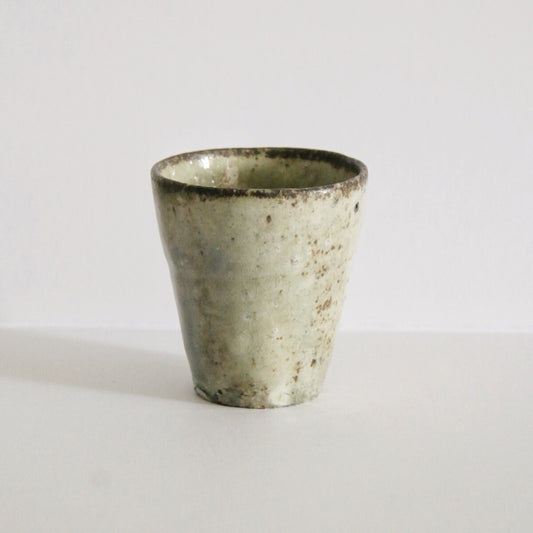 Tapered cup in mottled cream and soft green with a lightly speckled surface, on white.