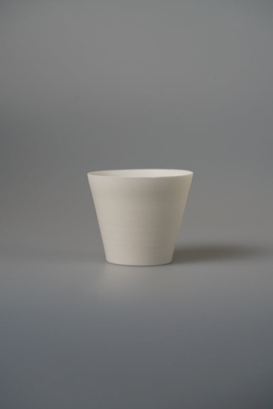 Small tapered white porcelain cup with clean straight sides, on a pale grey ground.
