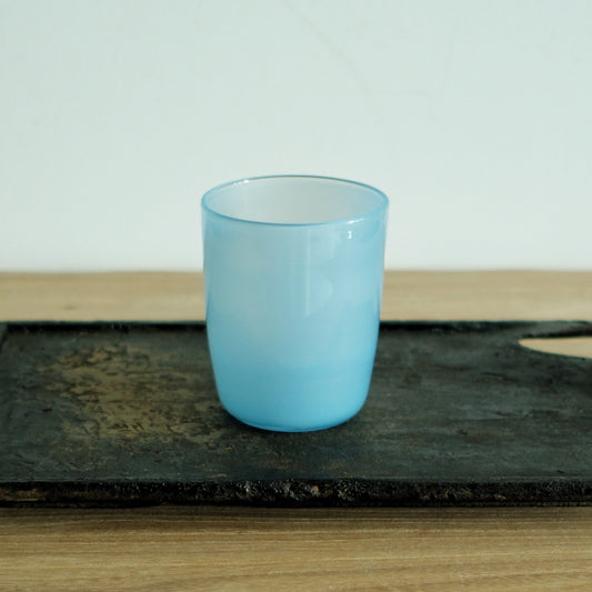 Opaque glass cup in soft sky blue, standing on a dark weathered board.