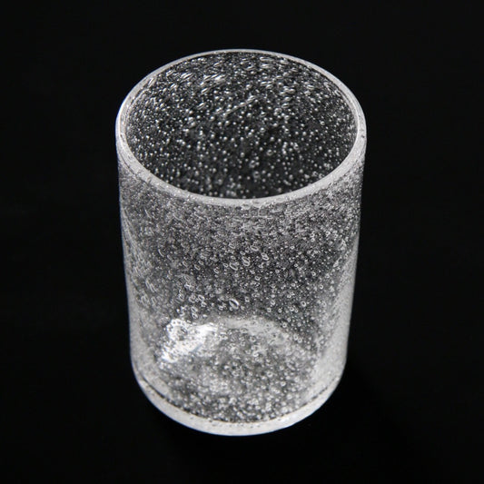Straight clear glass tumbler filled with a dense veil of tiny trapped bubbles, on black.