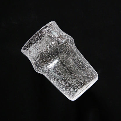 Tall waisted clear glass tumbler dense with tiny bubbles, tilted against a black ground.