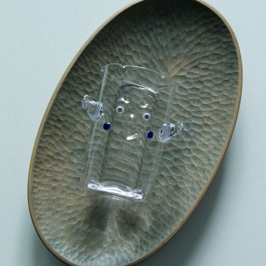 Clear glass cup with a small applied glass creature clinging to its side, on a green dimpled plate.