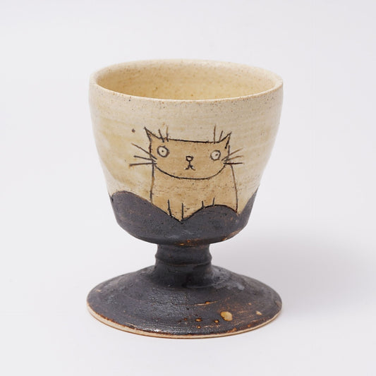 Cream stemmed cup drawn with a simple line cat, standing on a dark speckled pedestal foot.