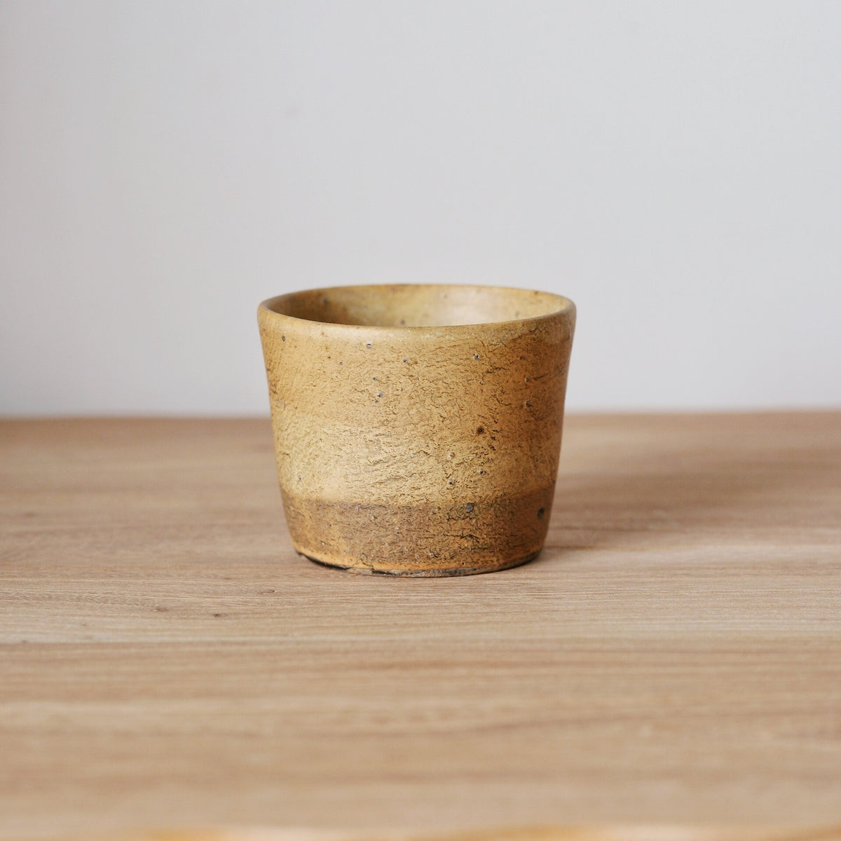 Straight-sided cup in warm sandy brown with a rough grainy surface, on a wooden table.