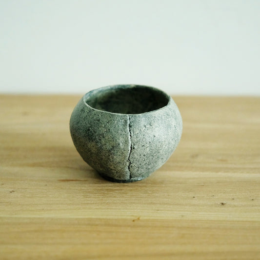 Round grey cup with a coarse stone-like surface and a deep crack line running down one side.