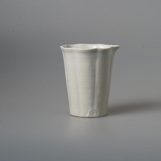 Tall white pouring vessel with softly fluted sides and a folded lip, on pale grey.