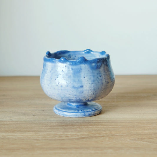 Stemmed cup in mottled cornflower blue with a softly frilled rim, on a wooden table.