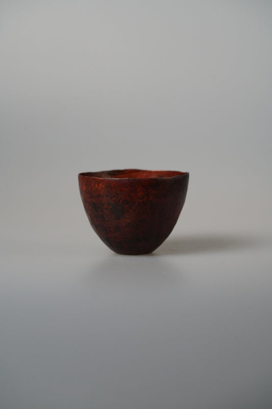 Small footed metal cup in oxidised copper, deep red-brown with a mottled surface.