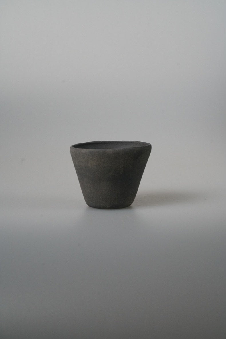 Small conical cup in matte charcoal black with straight flaring sides, on pale grey.