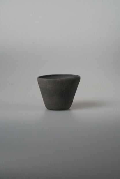 Small conical cup in matte charcoal black with straight flaring sides, on pale grey.