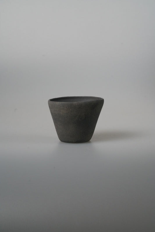 Small conical cup in matte charcoal black with straight flaring sides, on pale grey.