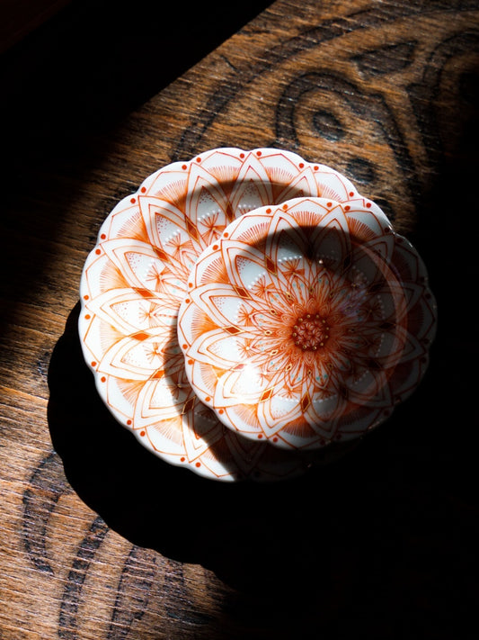 Two small white dishes painted in fine red line-work with a radiating floral pattern, lit in low sun.