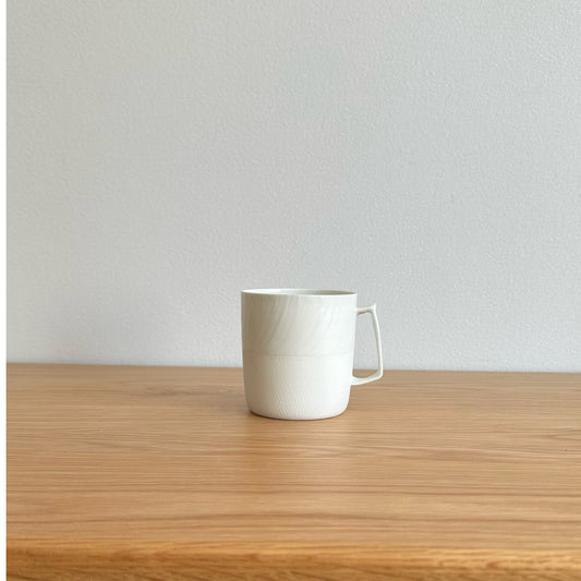 Plain white mug with straight sides and a squared handle, on a light wooden table.