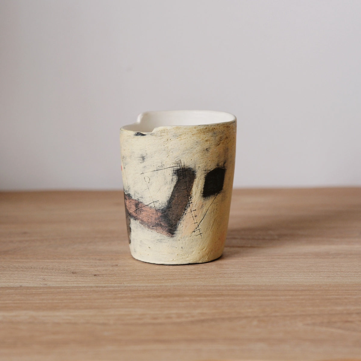 Tapered cream cup with a rough speckled surface and dark abstract marks brushed on one side.