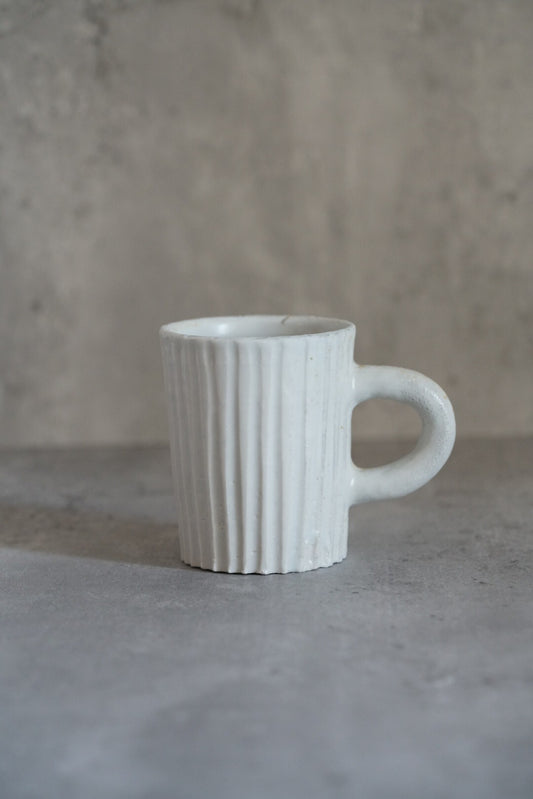 Tall white mug with close vertical ribbing and a large open ring handle.