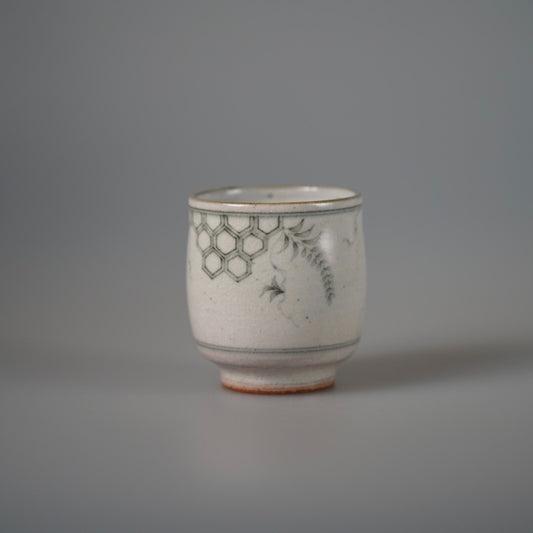 Cream cup painted in blue with a honeycomb band and fine leafy sprays, on a rust foot.