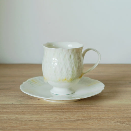 White porcelain cup with a quilted diamond texture, standing on a matching saucer edged in soft yellow.