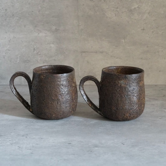 Two rounded mugs in mottled rust brown with rough surfaces and small loop handles.