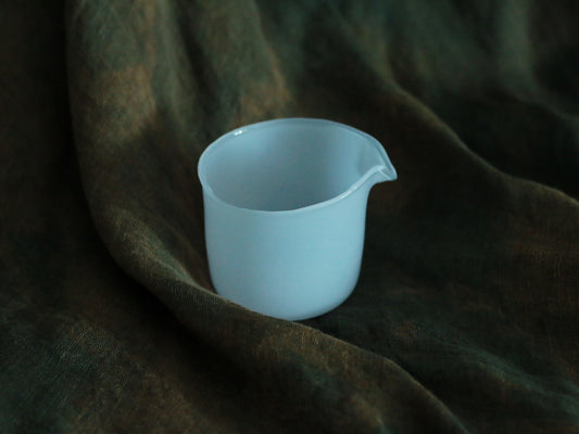 Small opaque glass pourer in soft sky blue with a drawn lip, on dark green cloth.