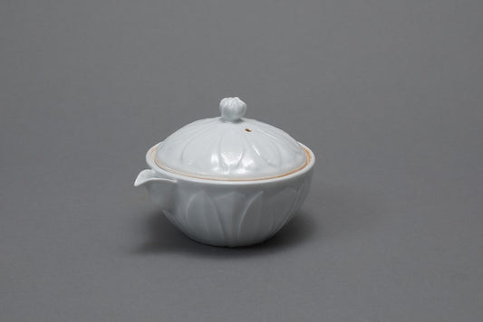 Small white porcelain lidded teapot with lotus-petal fluting and a thin amber line at the rim.