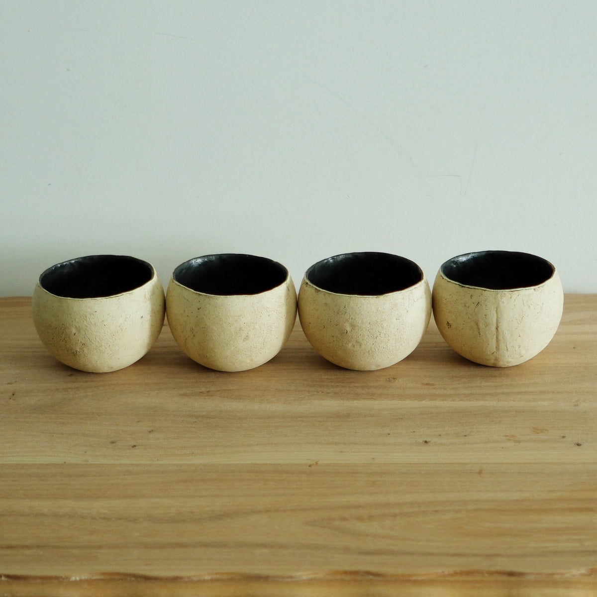 Four round cream cups with crusty surfaces and deep black interiors, lined up on a wooden shelf.