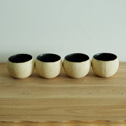 Four round cream cups with crusty surfaces and deep black interiors, lined up on a wooden shelf.