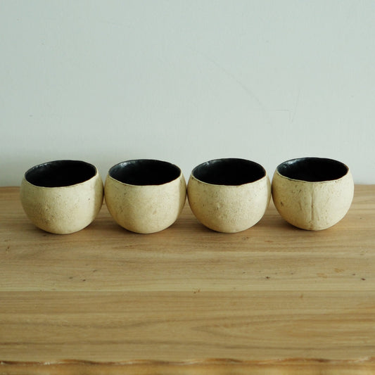 Four round cream cups with crusty surfaces and deep black interiors, lined up on a wooden shelf.