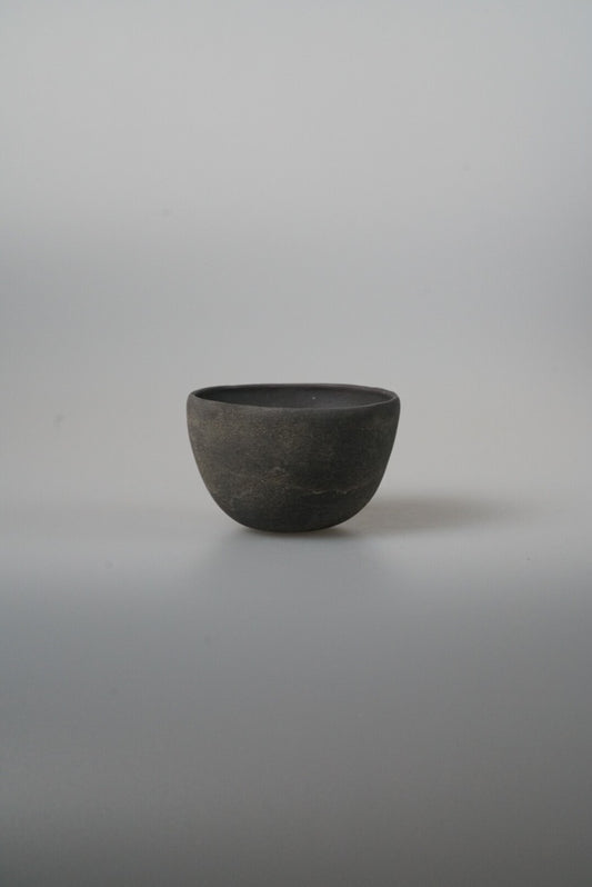Small deep bowl in matte charcoal black with a softly rounded profile, on pale grey.