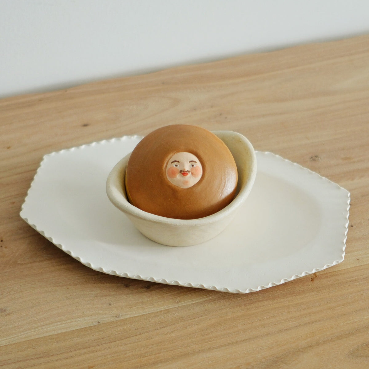 Ceramic pancake sandwich in warm brown with a painted face, sitting in a small cream bowl.
