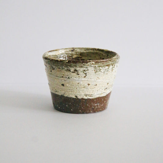 Squat tapered cup with white slip brushed over rust-brown clay and an unglazed clay foot.
