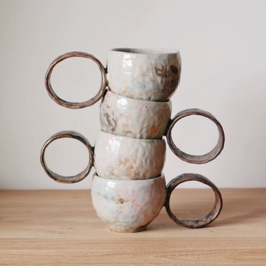 Four rough white mugs stacked in a tower, their large open ring handles jutting out to the sides.