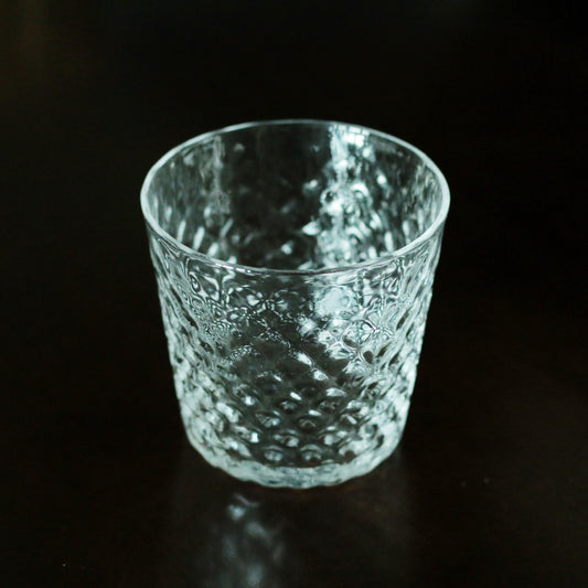 Pale green glass tumbler with a finely pebbled surface, glowing against a black background.