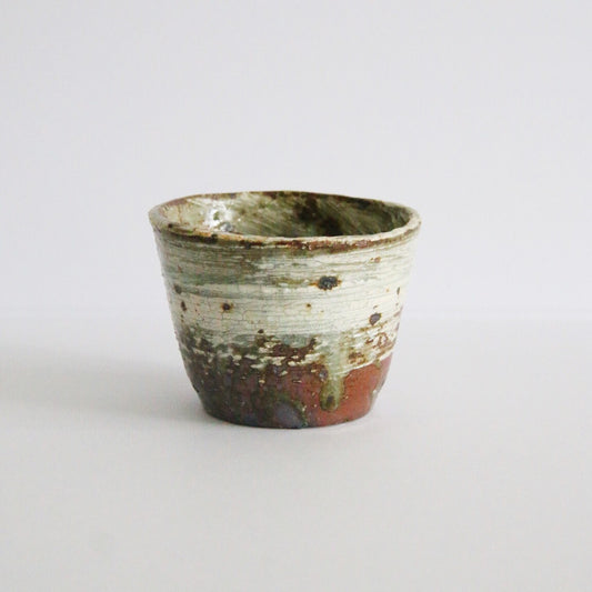 Tapered cup with white slip brushed over rust-brown clay, the bare clay showing at the foot.