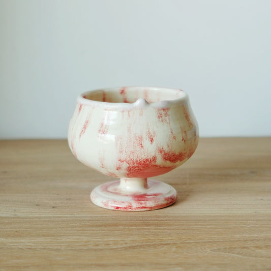 White stemmed cup splashed with soft red flecks, on a light wooden table.