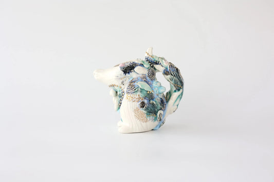 Small white sculptural tea pitcher topped with a modelled squirrel, painted in soft blue and green marks.
