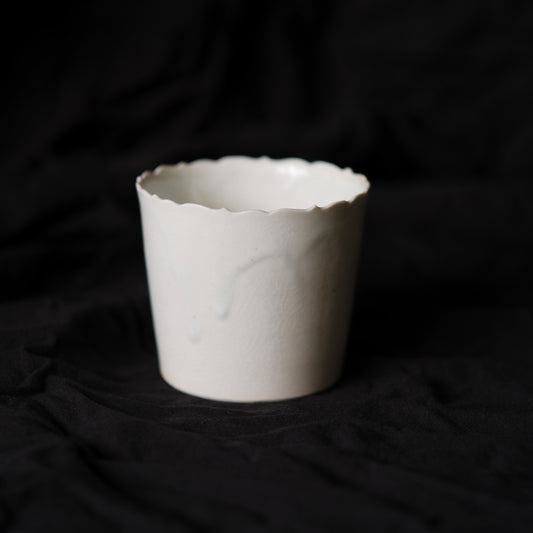 Straight-sided white porcelain cup with a softly torn scalloped rim, on black cloth.