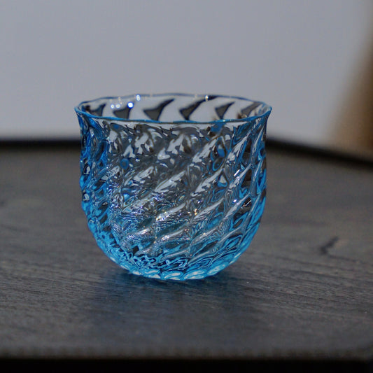 Bright blue glass tea cup with a deeply cut diamond-scale surface, on a dark table.